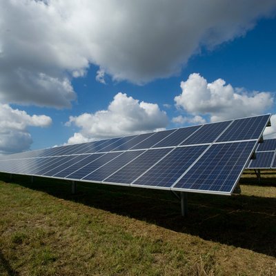 Outdoor view, low perspective, panels in a green field, fluffy white clouds