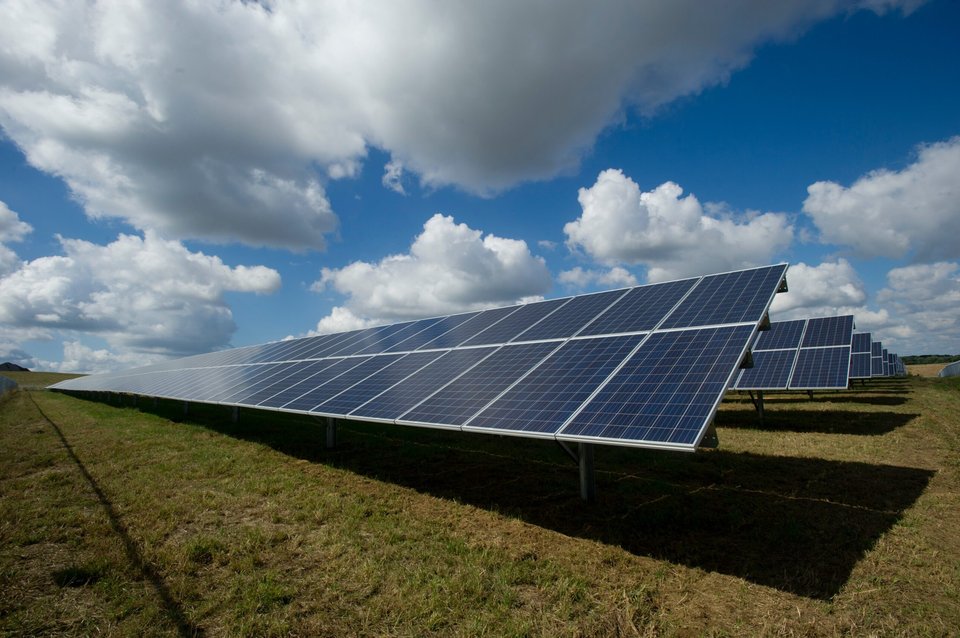 Outdoor view, low perspective, panels in a green field, fluffy white clouds