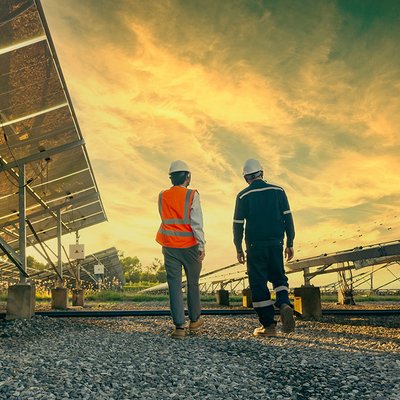 Two workers walking along a series of panels in a field, low perspective, sunrise or sunset